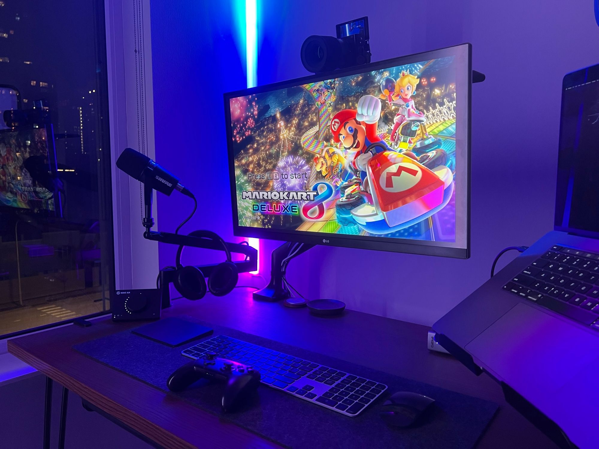 A view of the desk at night with a Nintendo Switch controller in front of the keyboard and Mario Kart displayed on the monitor.